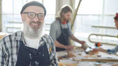 A photo of a man smiling at work with two other workers working behind him.