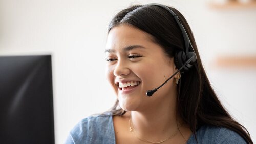 Young woman working in claims support center takes calls on headset while looking at computer screen