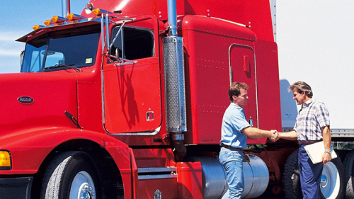 Two men shaking hands in front of a semi truck.