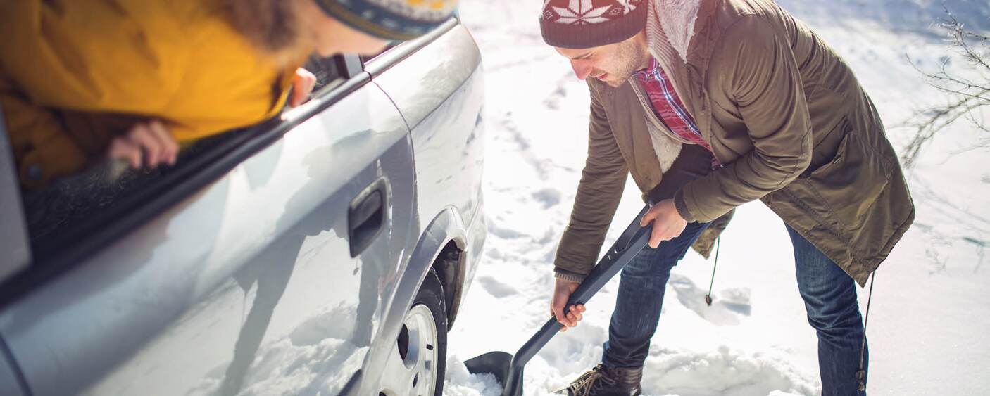 A mans car is stuck in the snow so he's trying to shovel it out.