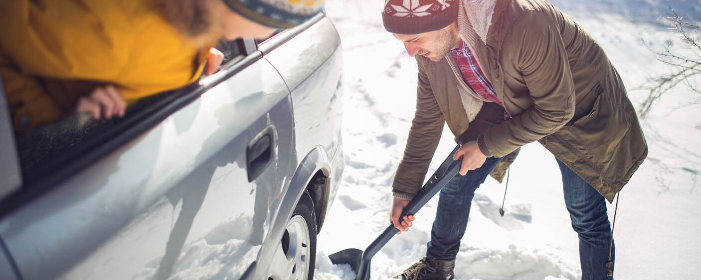 A mans car is stuck in the snow so he's trying to shovel it out. 