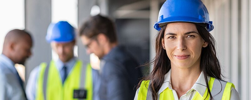 A woman smiling with a yellow vest and hard at on.