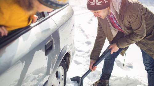 A mans car is stuck in the snow so he's trying to shovel it out. 