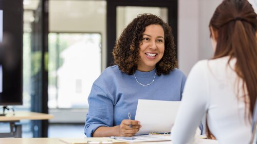 Two females sitting at a table, with one of them interviewing the other.