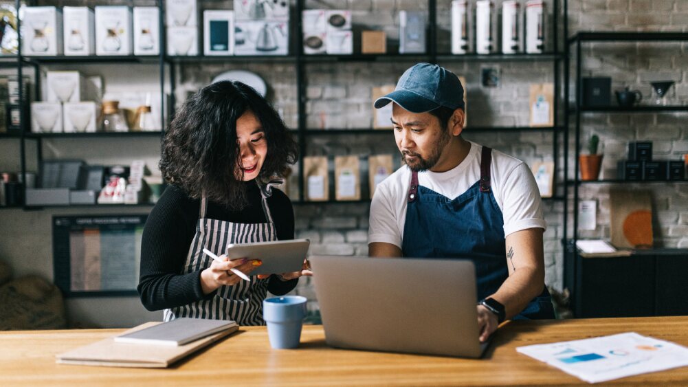 two small business owners reviewing data on a laptop and tablet.