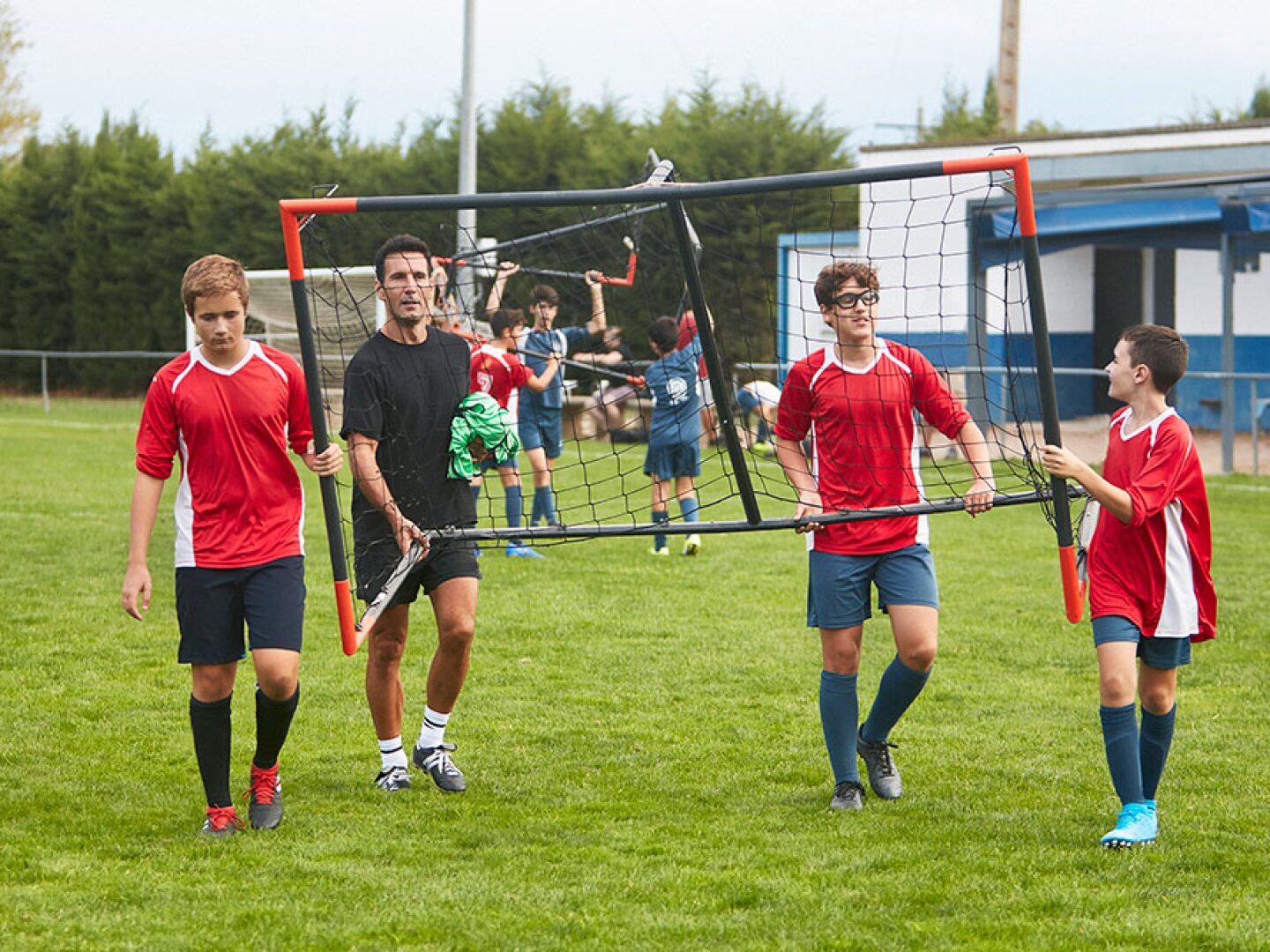 soccer coach and teammates carrying goal equipment onto the field for practice