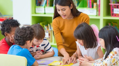 A daycare provider/teacher helping her students read.