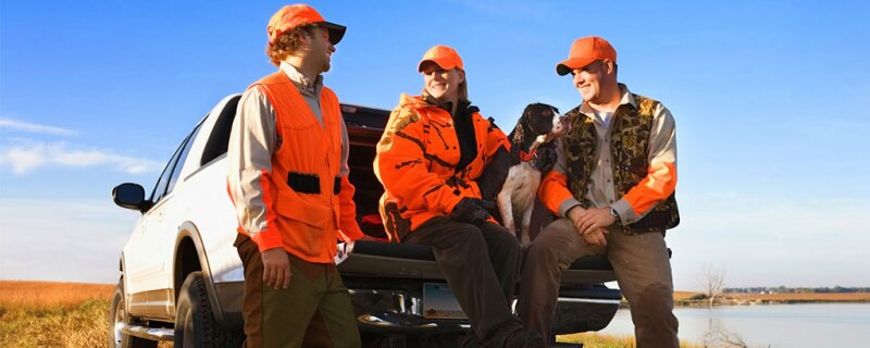 Three people and a dog outside in their hunting gear.
