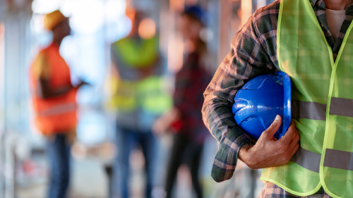 A man holding a hard helmet with a yellow vest on.