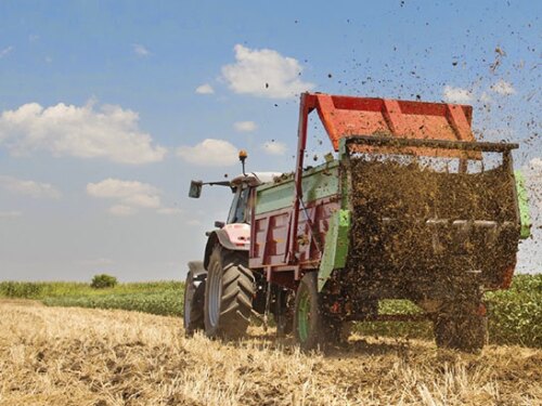 Farmer driving a tractor spreading manure.