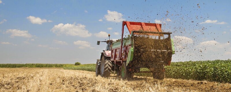 Farmer driving a tractor spreading manure.