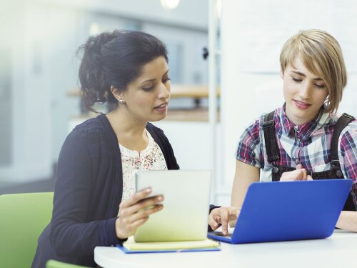 A women and younger female looking at a laptop while the women teachers the young female.