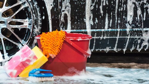 Car with soap on it and a bucket with cleaning supplies.
