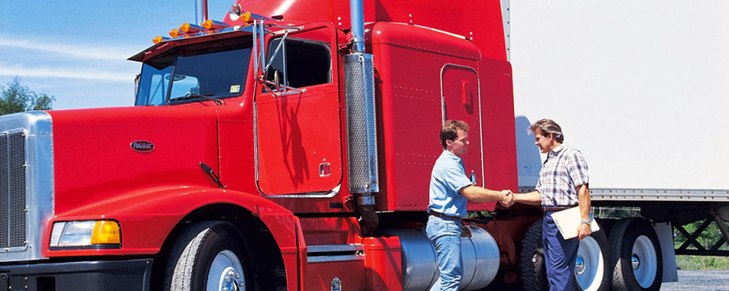 Two men shaking hands in front of a semi truck.
