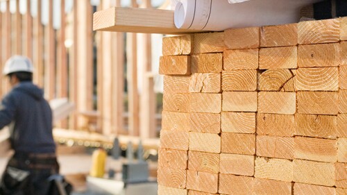 Picture of a pile of wood with someone in the back carry pieces of wood. 