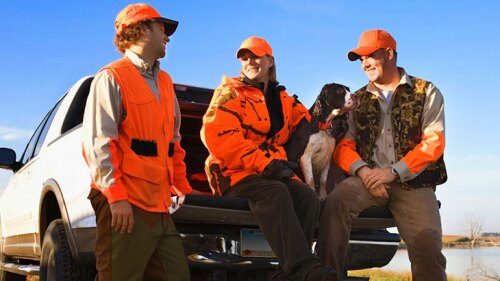 Three people and a dog outside in their hunting gear.
