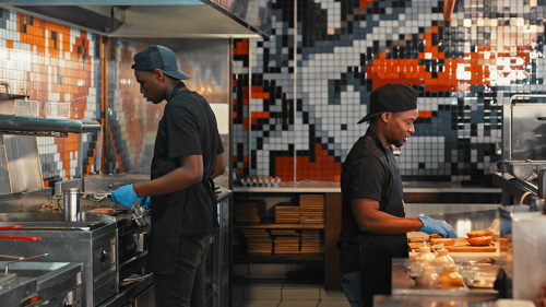 Two chiefs preparing food in a restaurant kitchen.
