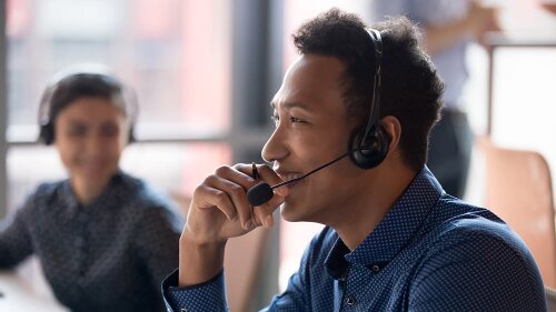 Smiling young male call center agent smiling while taking a support call at work