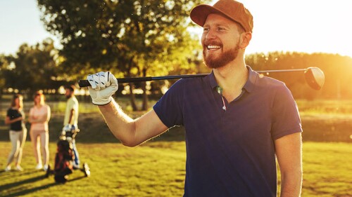 A man smiling while holding his golf club on a golf course.