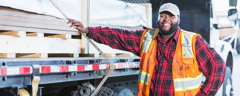 A man standing in front of his semi truck that is loaded. 