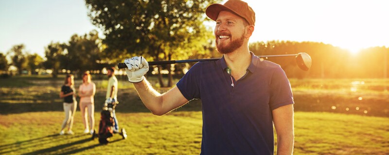 A man smiling while holding his golf club on a golf course.