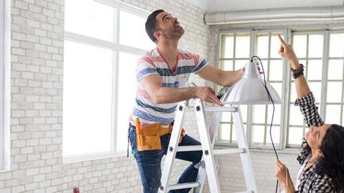 A man standing on a ladder about to hang up a light.