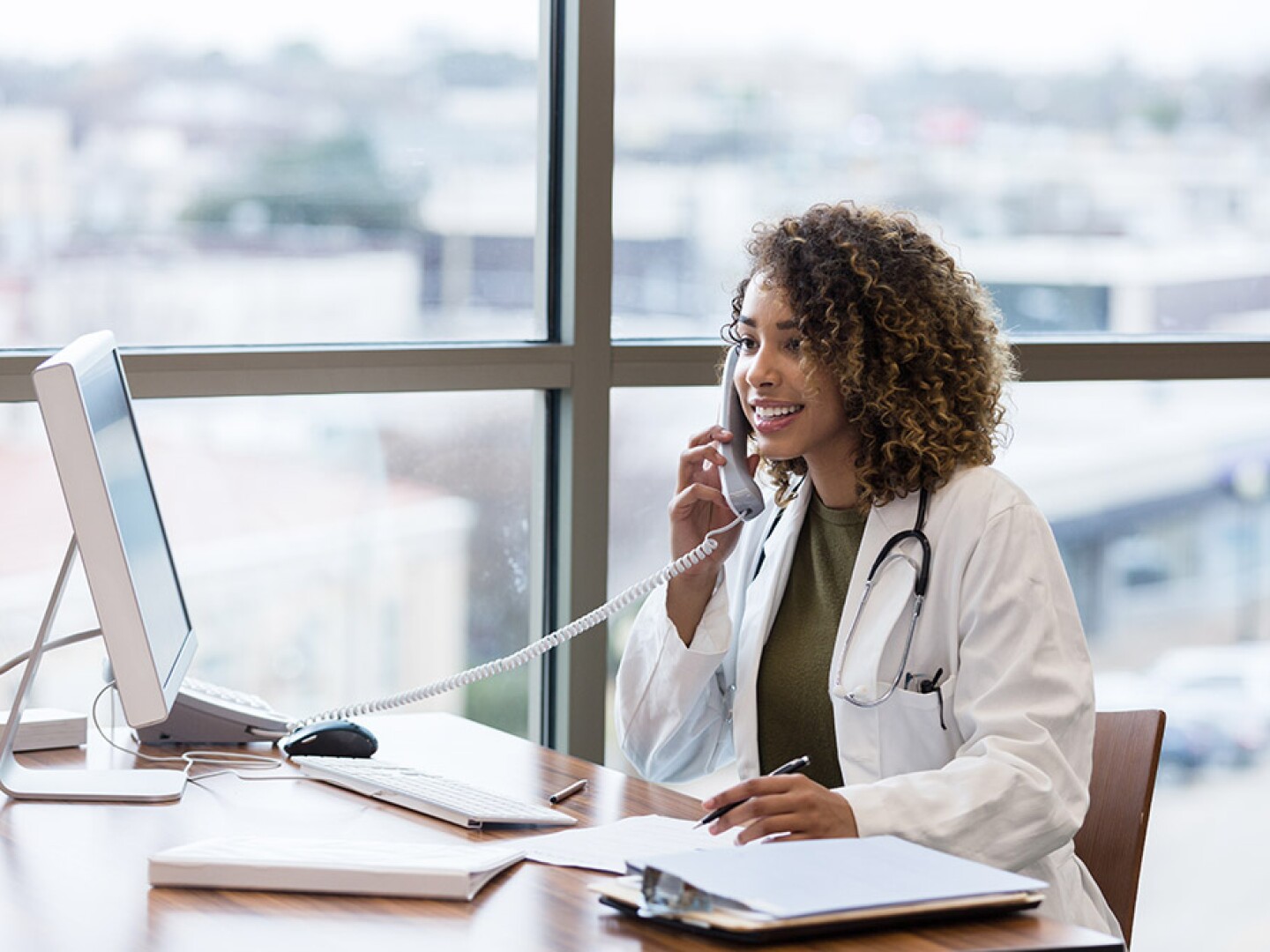 A young adult female doctor talks with a patient on the phone.