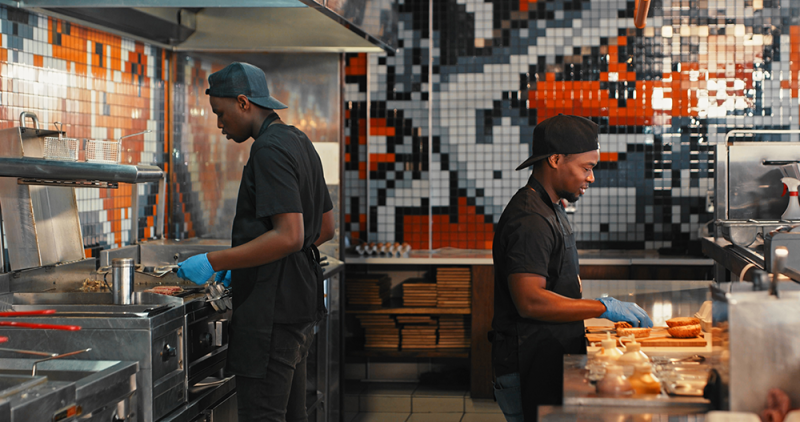 Two chiefs preparing food in a restaurant kitchen.